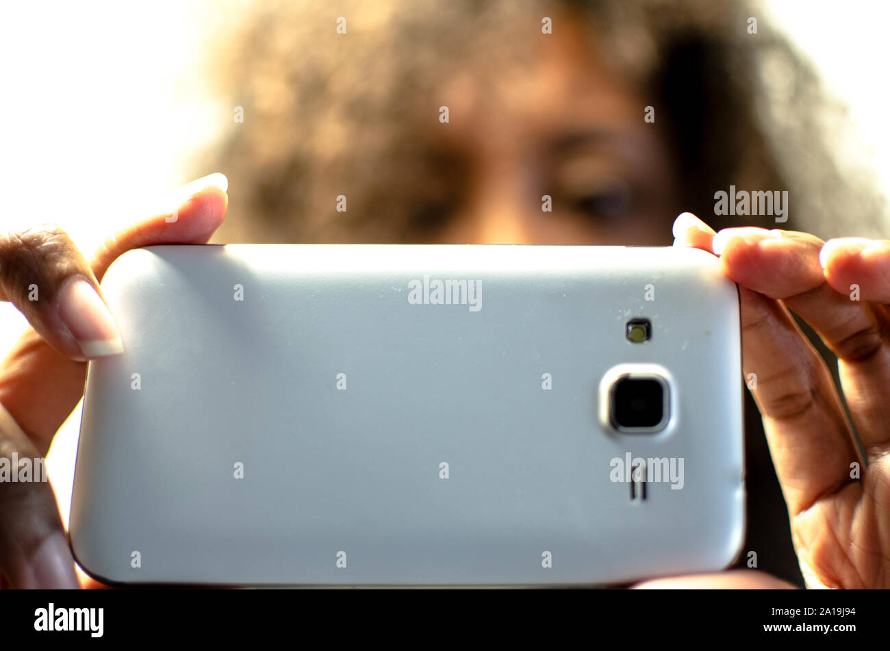Black woman taking a picture. Selective focus on foreground (smartphone and fingers) blurred background (person) Stock Photo