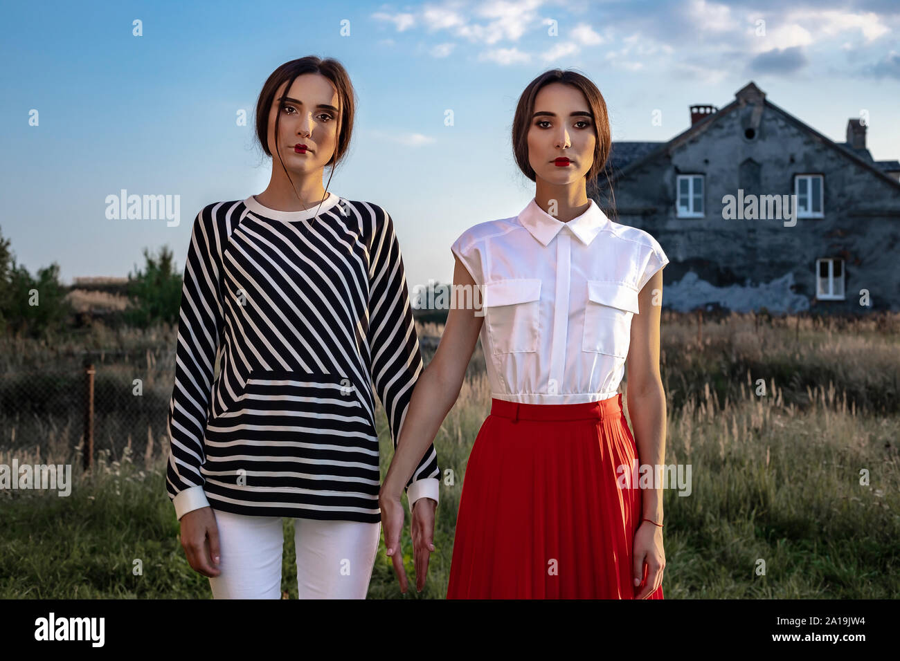 Outdoor fashion portrait of two young beautiful women wearing fashionable clothes posing on the street against the background of an old abandoned buil Stock Photo