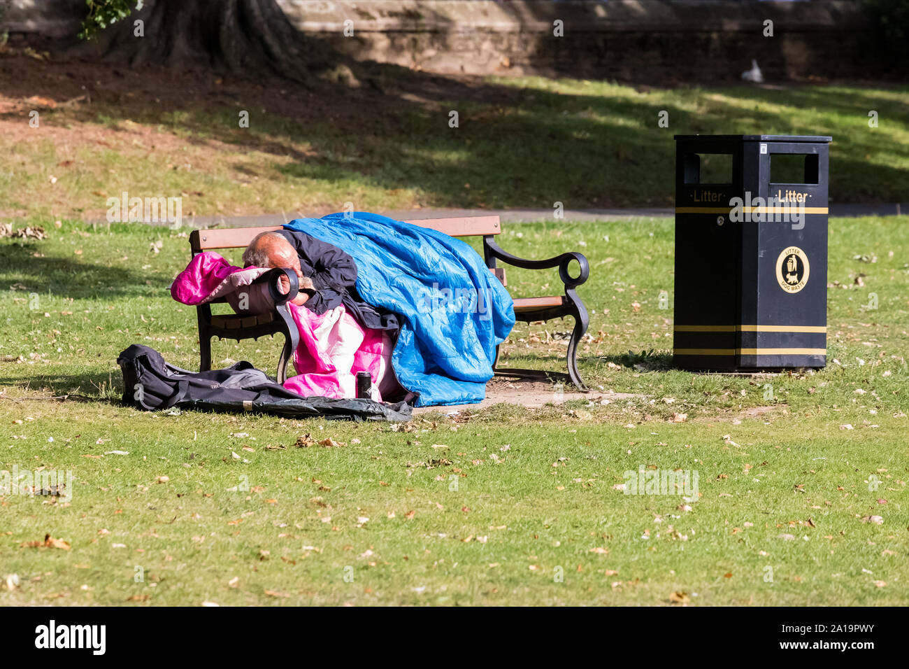Homeless man asleep in his sleeping bag on a park bench in the park Stock Photo
