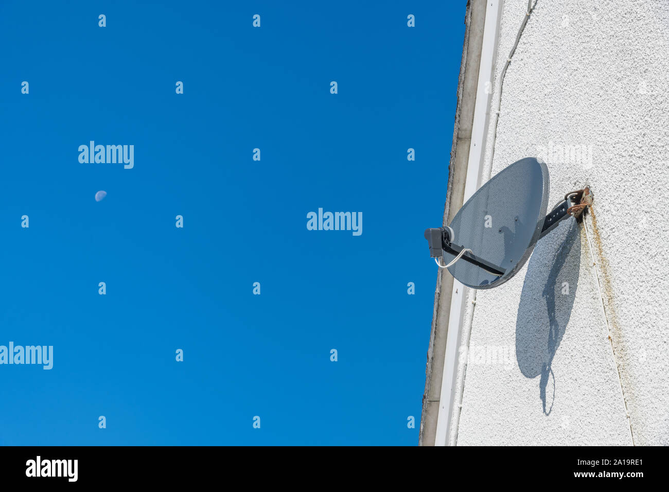 'Sky' branded parabolic TV satellite dish fixed to external wall. Set against blue sky with moon in background. Copy space & PIP space. Stock Photo