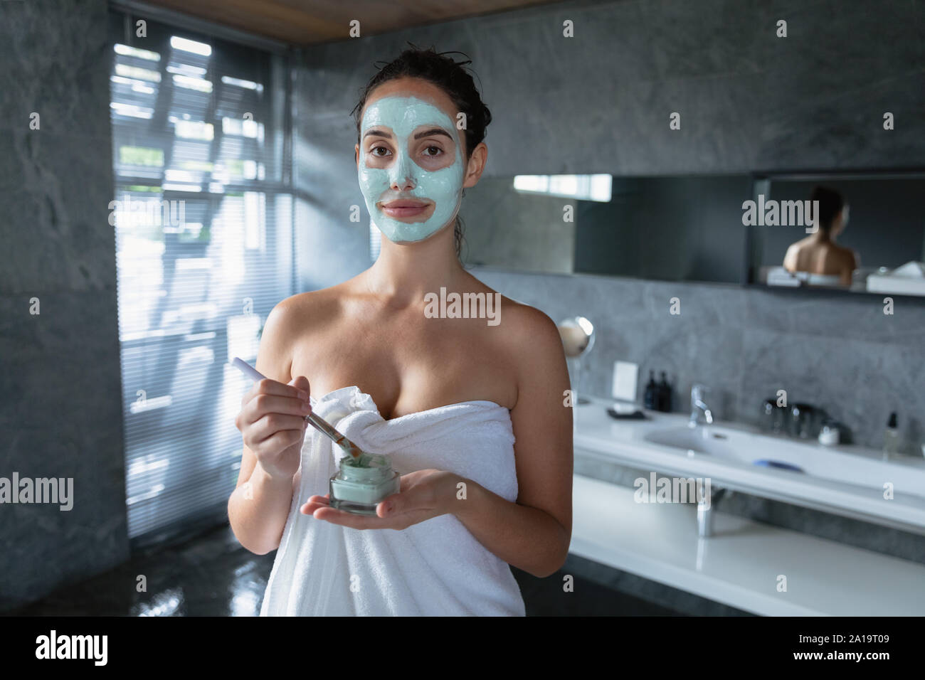 Portrait of young brunette woman applying face mask Stock Photo