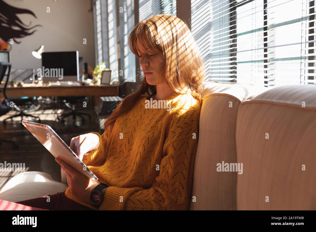 Young creative professional woman using tablet in a sunlit office Stock Photo
