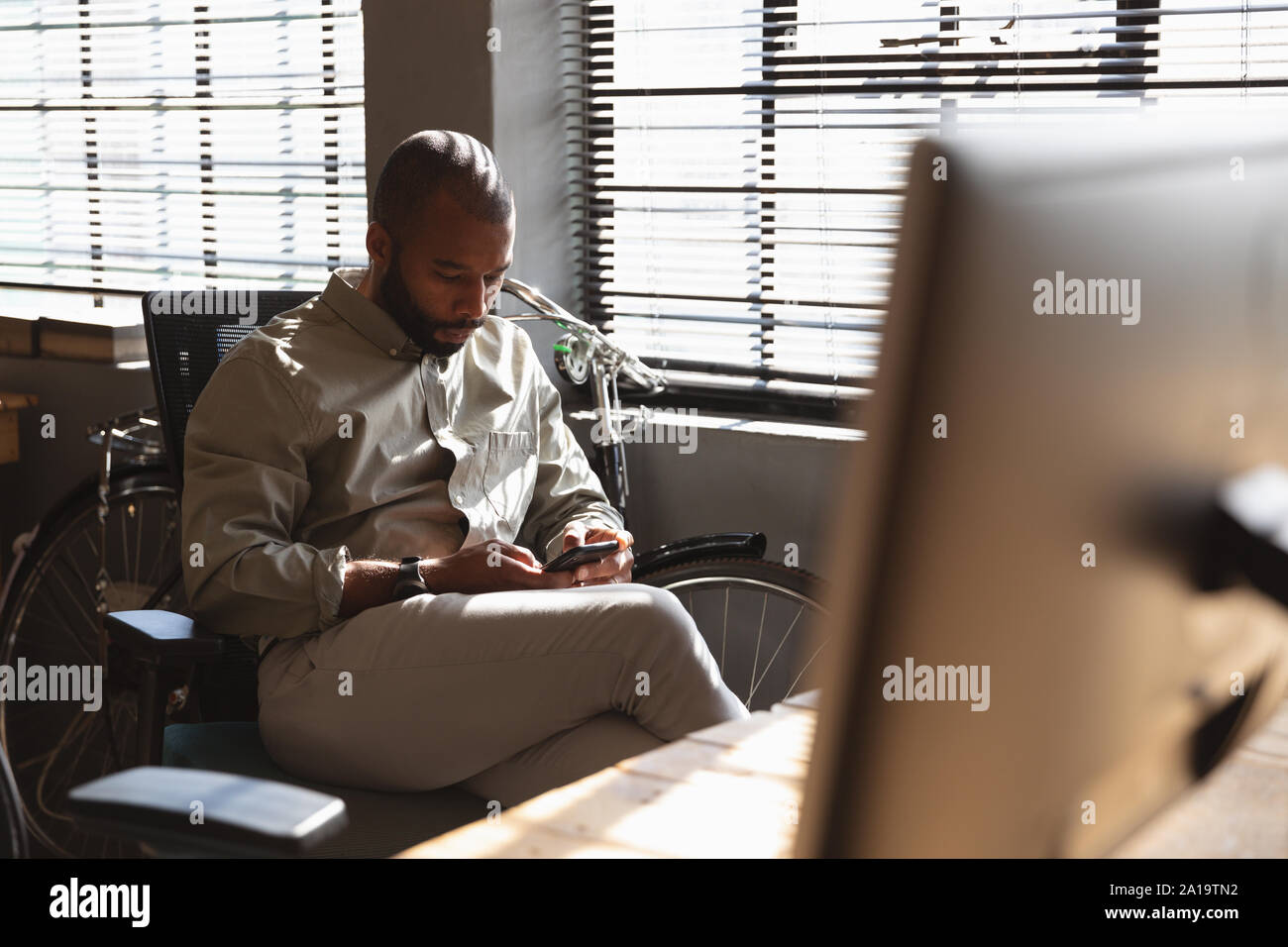 Young creative professional man using smartphone in a sunlit office Stock Photo