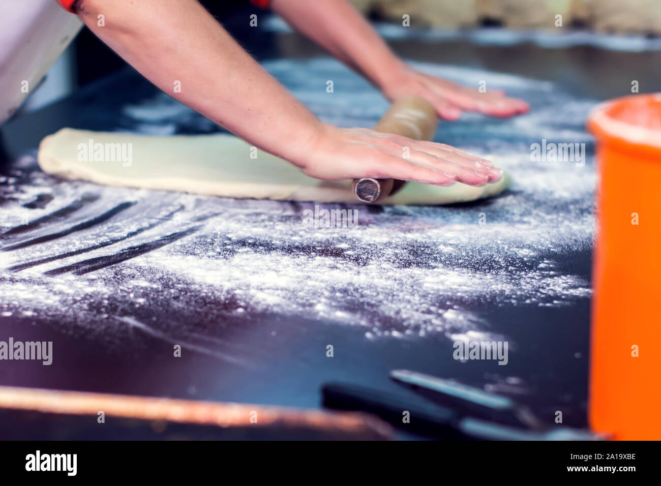 A chef rolls out the doughon on black table. Stock Photo
