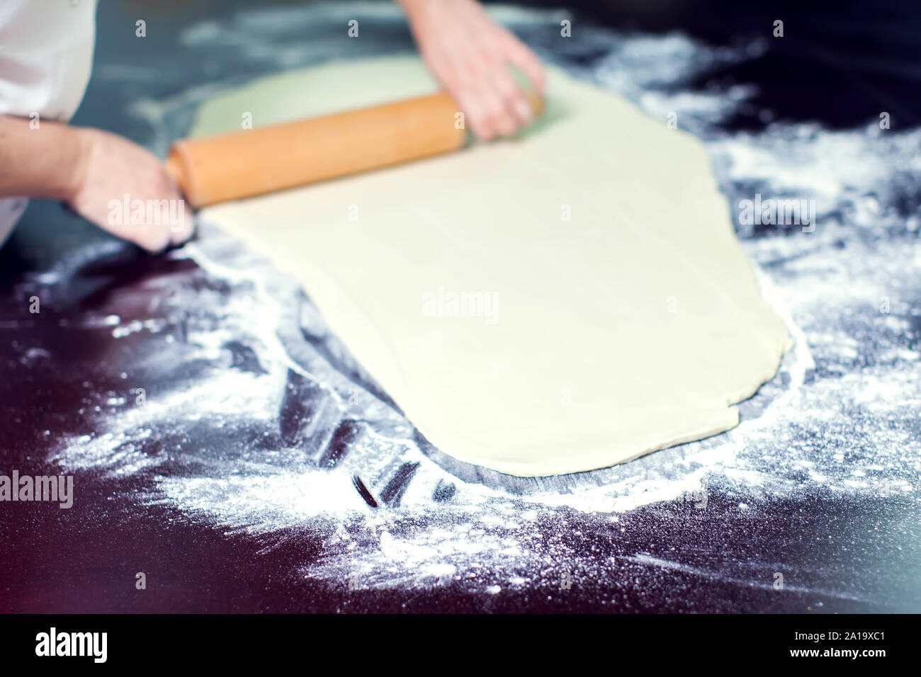 A chef rolls out the doughon on black table. Stock Photo