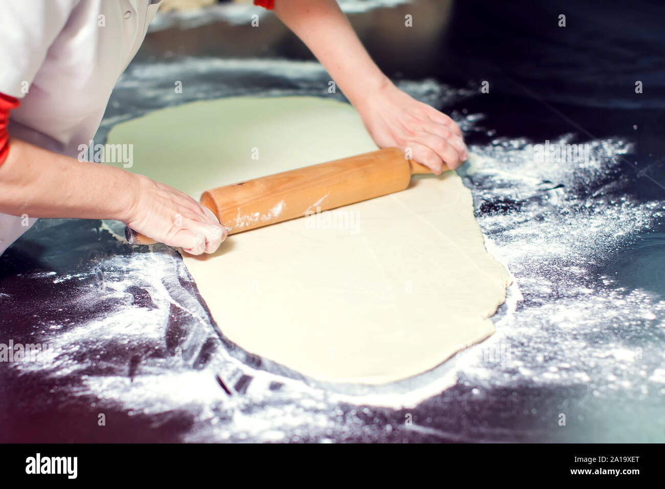 A chef rolls out the doughon on black table. Stock Photo