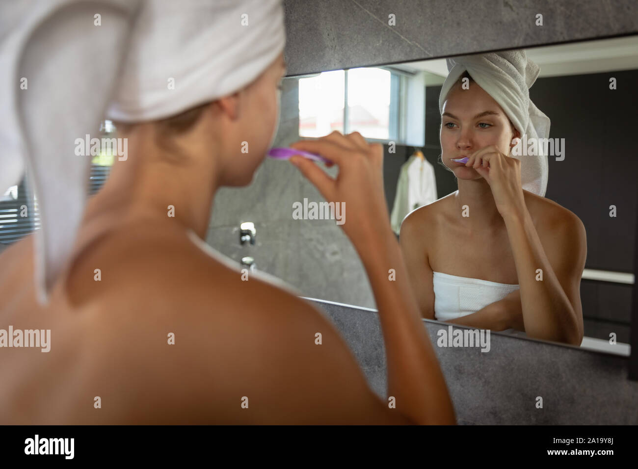 Young blonde woman brushing her teeth with her hair wrapped in a towel Stock Photo