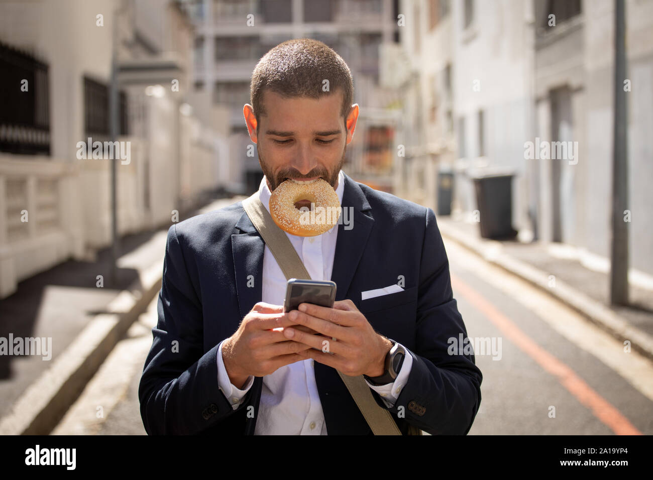 Young professional man eating a doughnut and using smartphone on the street Stock Photo