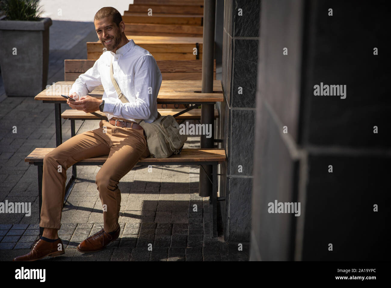 Young professional man using smartphone sitting outside Stock Photo