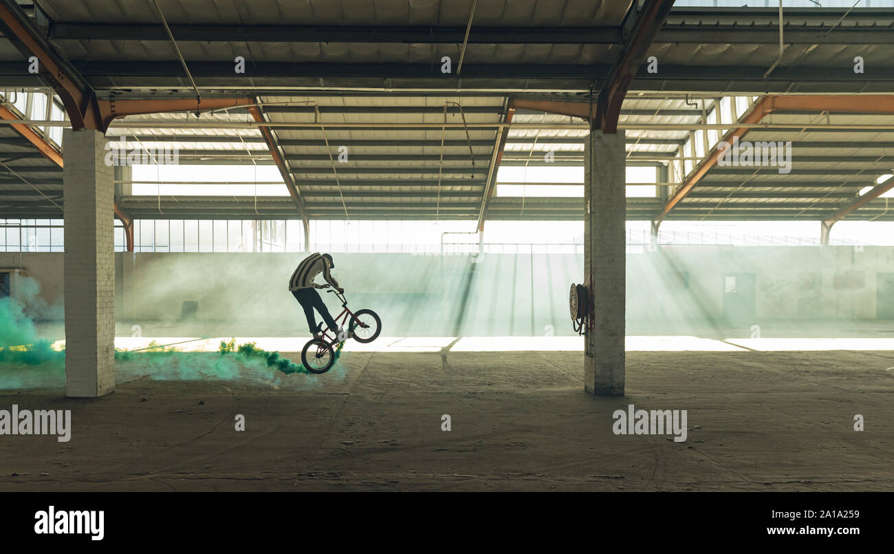 BMX rider in an empty warehouse using smoke grenade Stock Photo