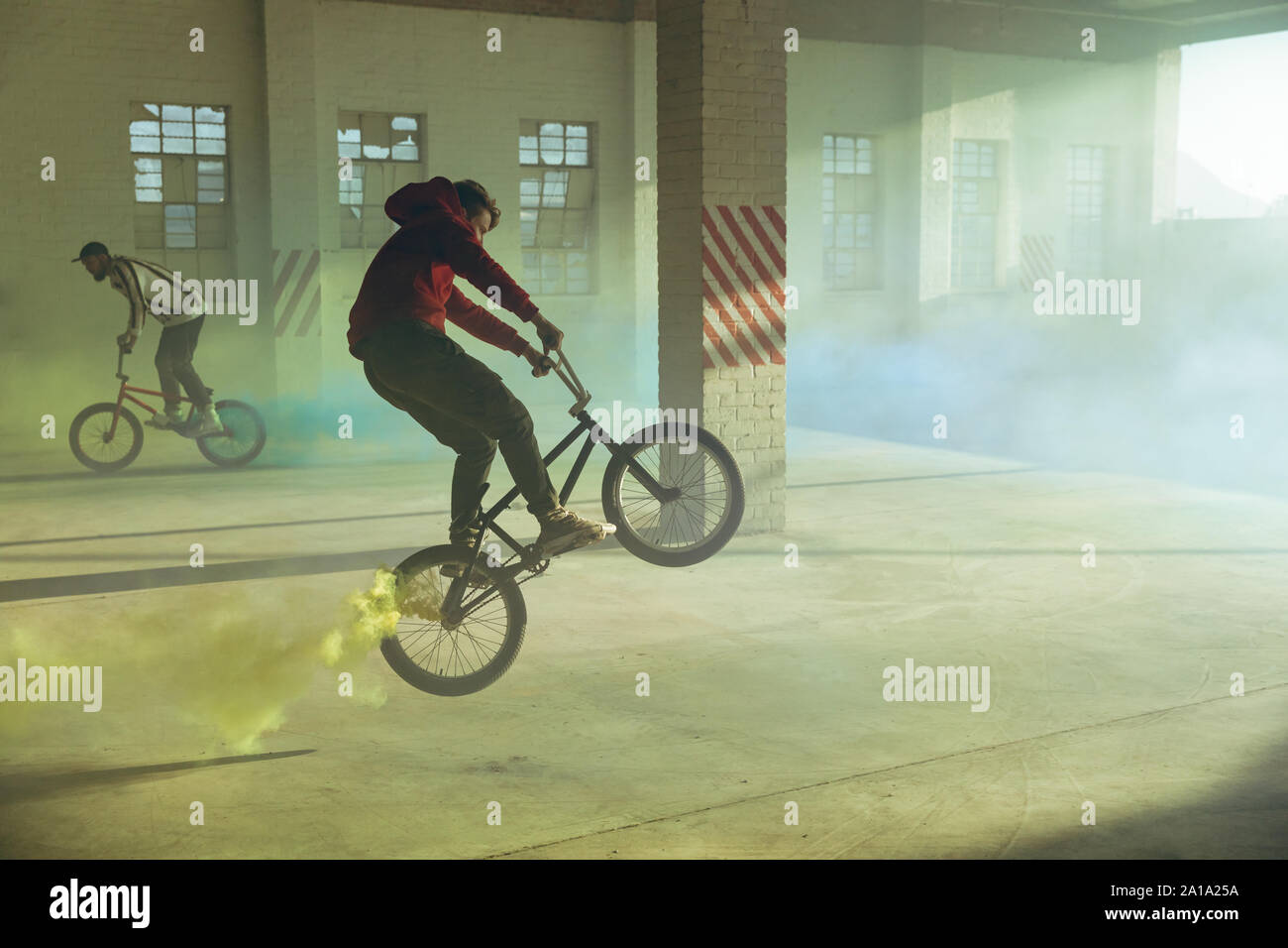 BMX riders in an empty warehouse using smoke grenades Stock Photo