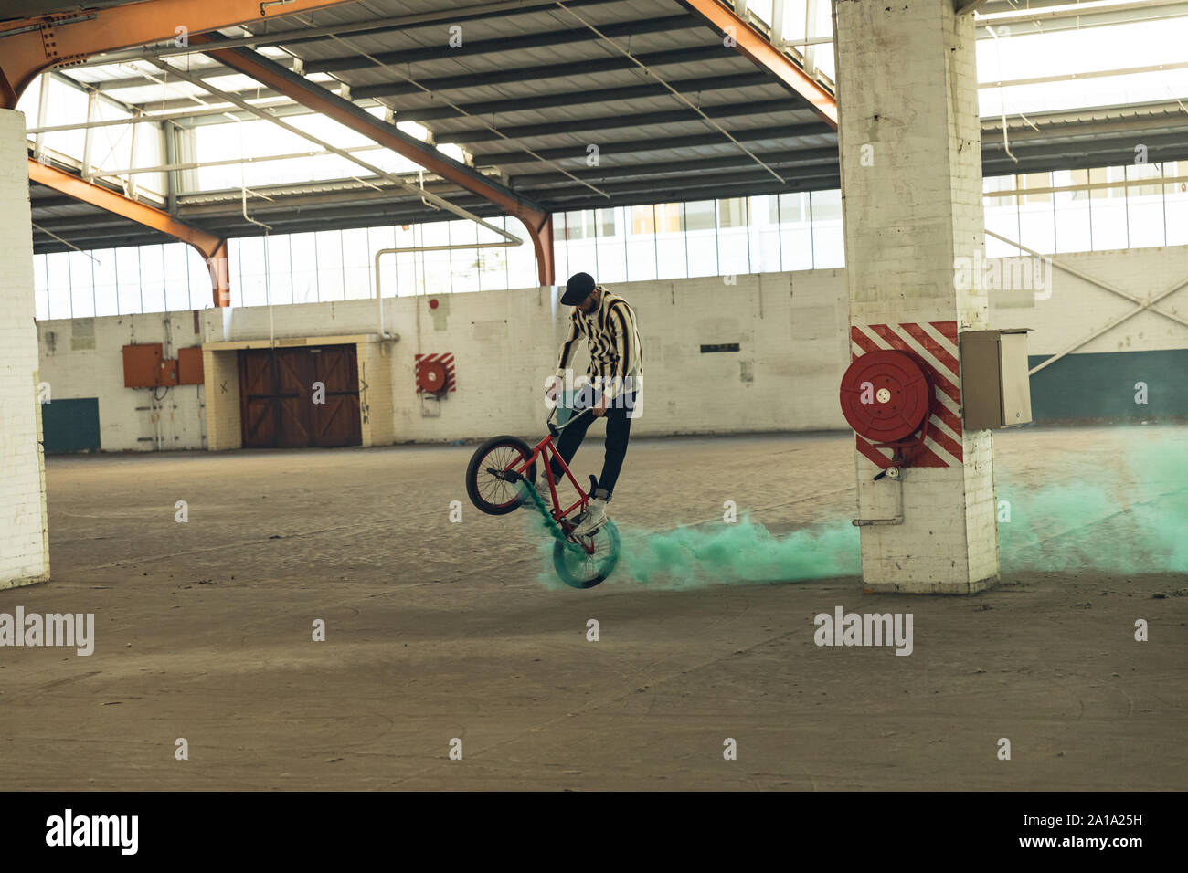 BMX rider in an empty warehouse using smoke grenade Stock Photo
