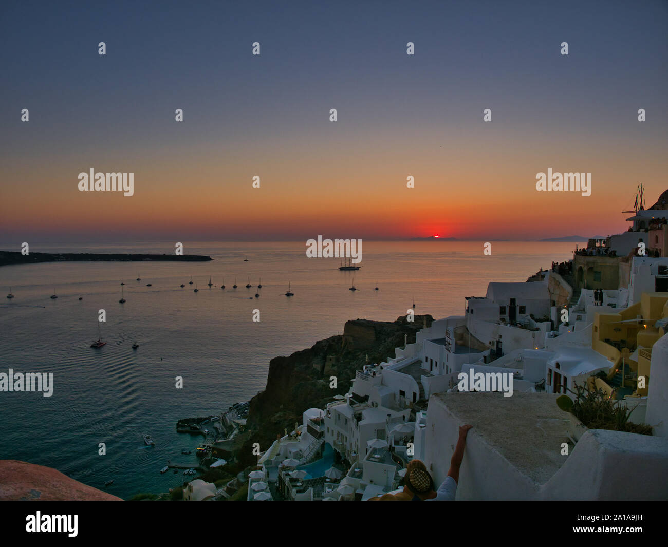 Majestic view of orange sun setting over tranquil water with boats and old town of Oia on Santorini island in Greece Stock Photo