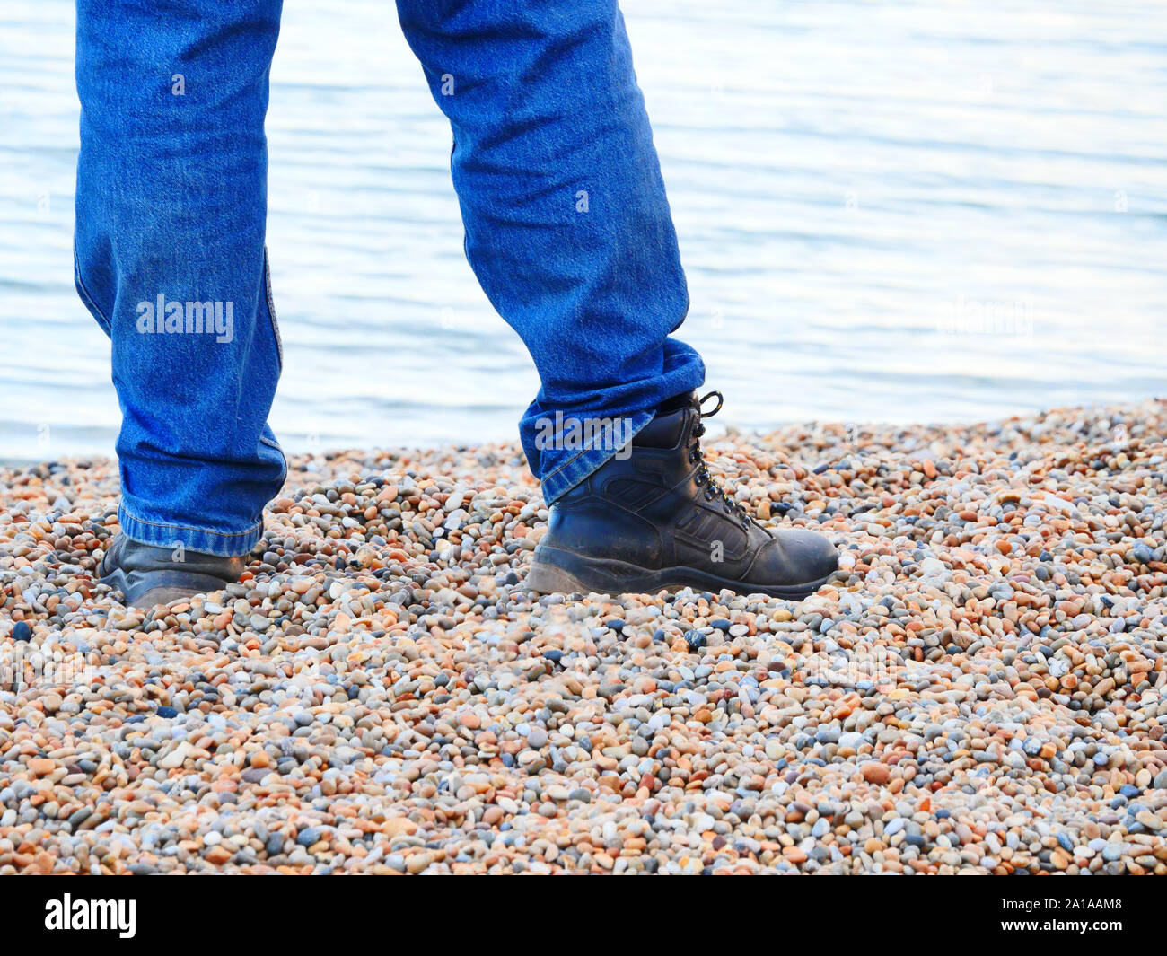 Legs and feet of man wearing boots standing on pebble beach, close up