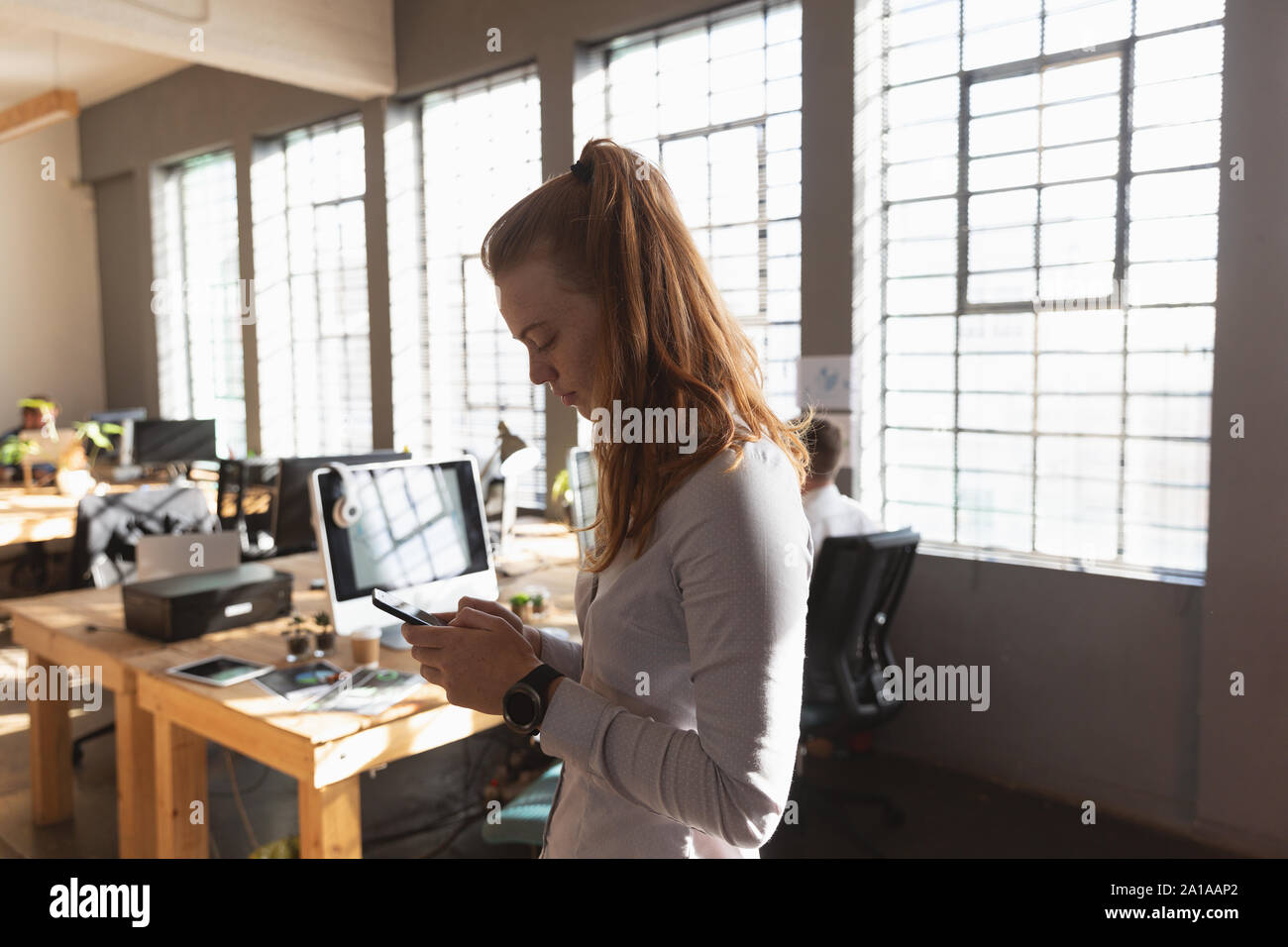 Young creative professional woman using smartphone  in a sunlit office Stock Photo