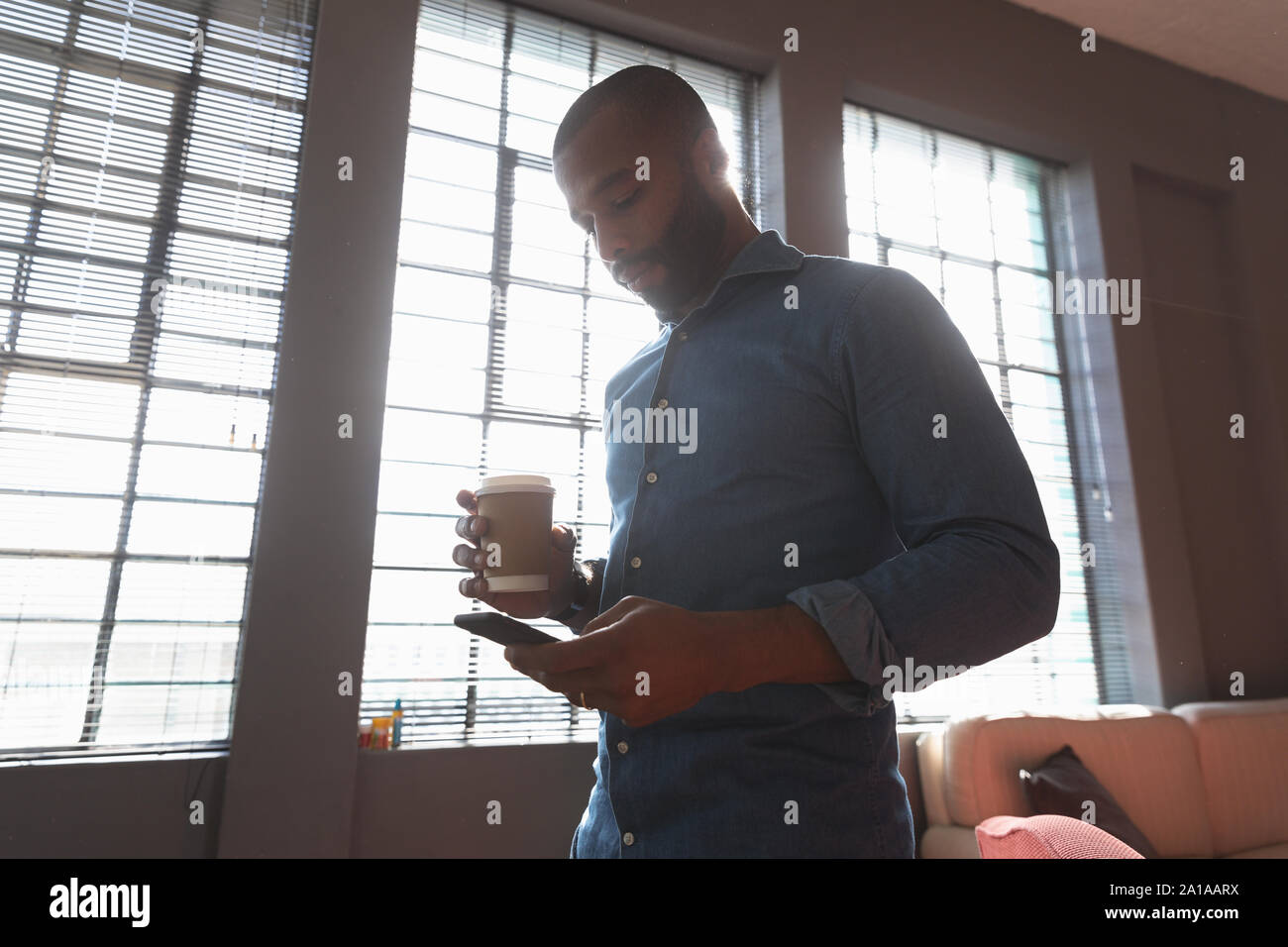 Young creative professional using smartphone in a sunlit office Stock Photo