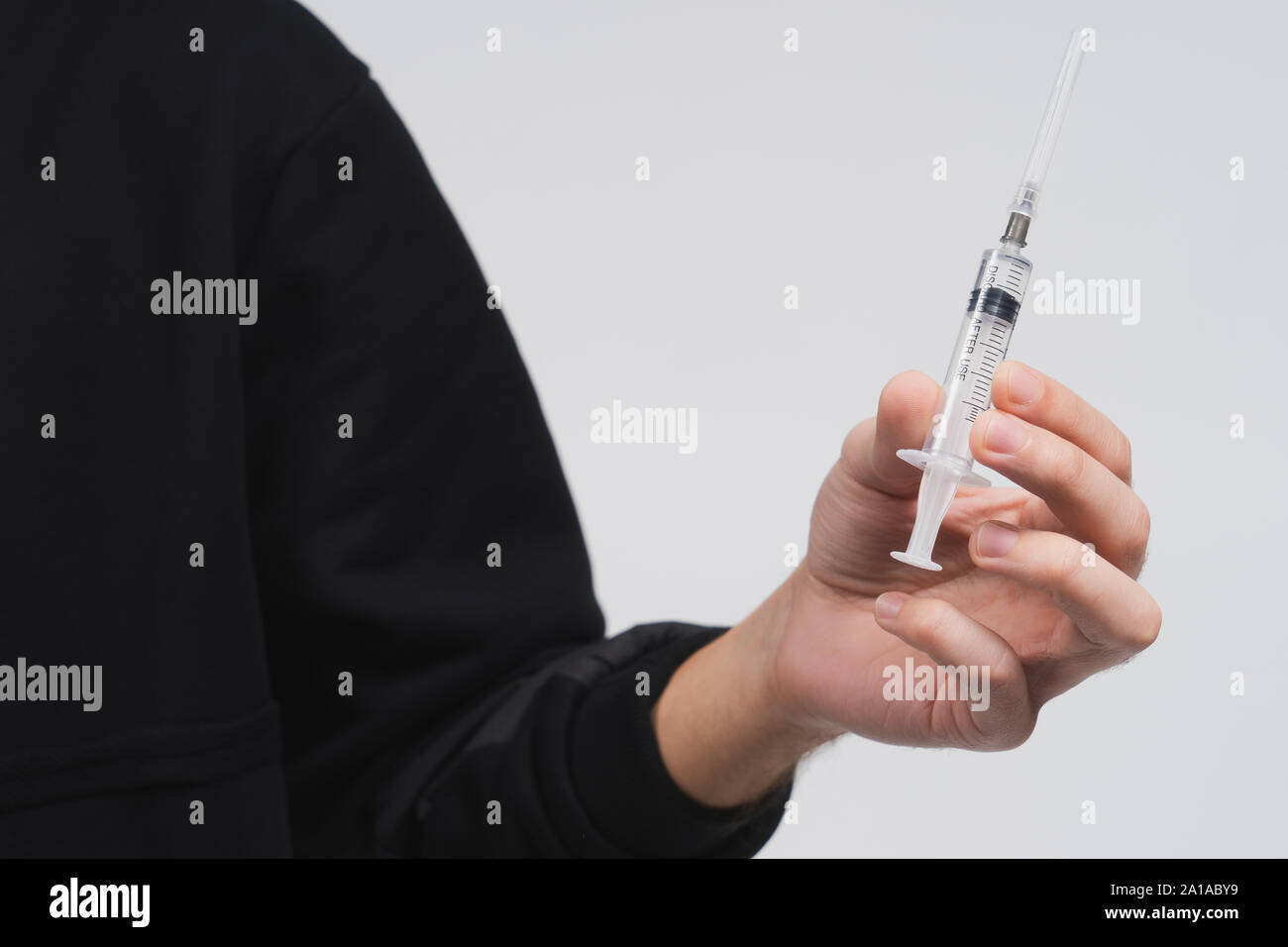 Man's hand hold a syringe with liquid. Guy in a black hoodie on a white background. Person offers you drug or medical treatment. Drug addict. Stock Photo