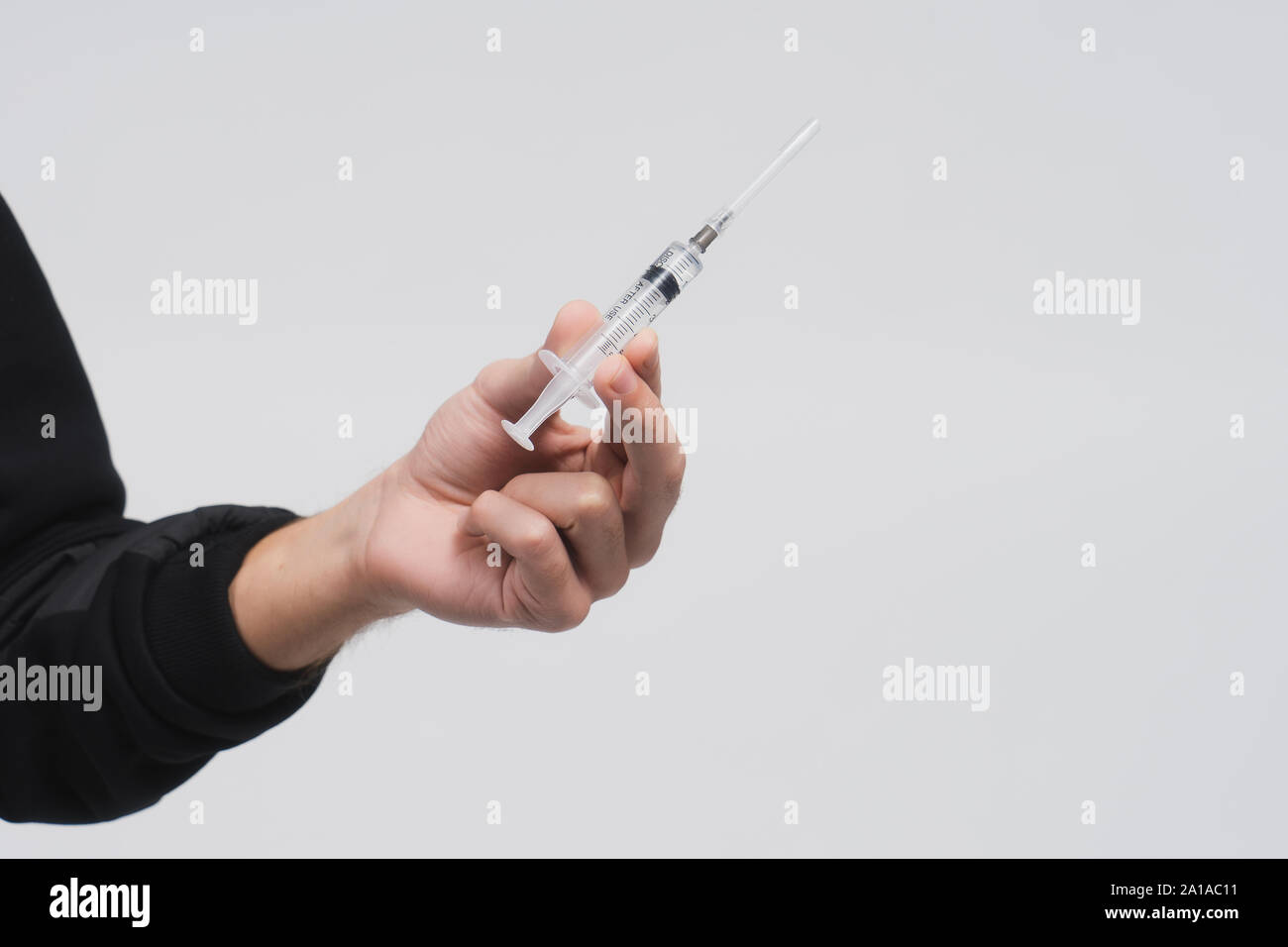 Man's hand hold a syringe with liquid. Guy in a black hoodie on a white background. Person offers you drug or medical treatment. Drug addict. Stock Photo