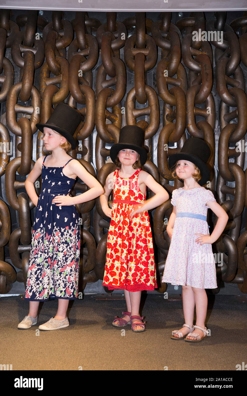 Three sisters children / kids / child / kid wearing top hat and pose in front of large chains to emulate the famous photograph of Isambard Kingdom Brunel taken by Robert Howlett. Taken at the Being Brunel exhibition accompanying the SS Great Britain ship, Dockyard, Bristol England UK (109) Stock Photo
