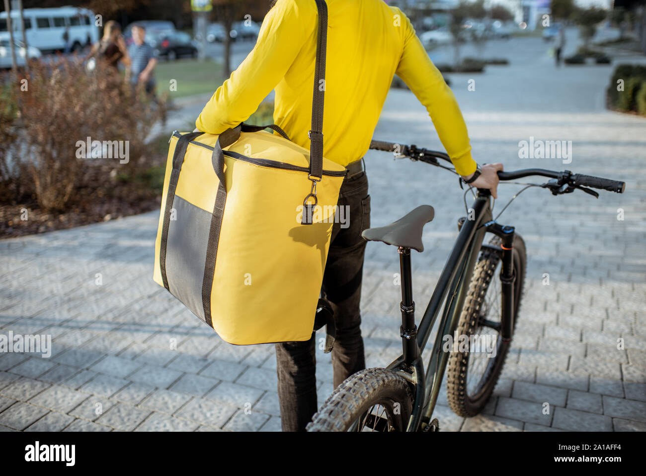 Courier delivering food in a yellow thermo bag with a bicycle in the