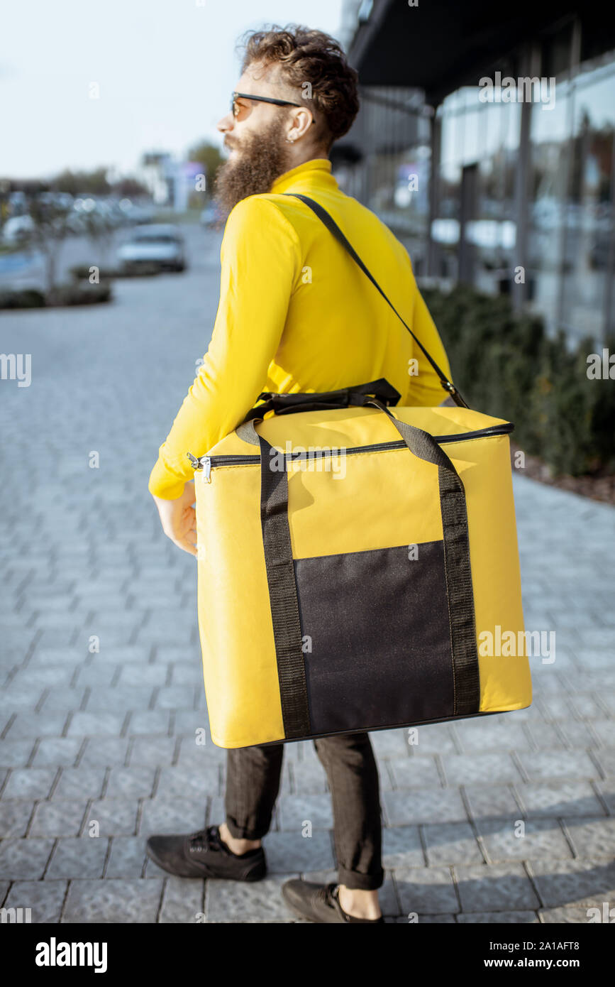 Young courier delivering food, walking with yellow thermal bag on the city  street. Delivery on foot concept Stock Photo - Alamy