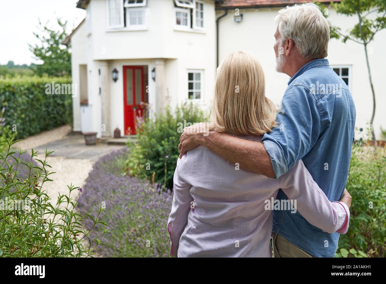 Rear View Of Mature Couple Standing In Garden Look At Dream Home In Countryside Stock Photo