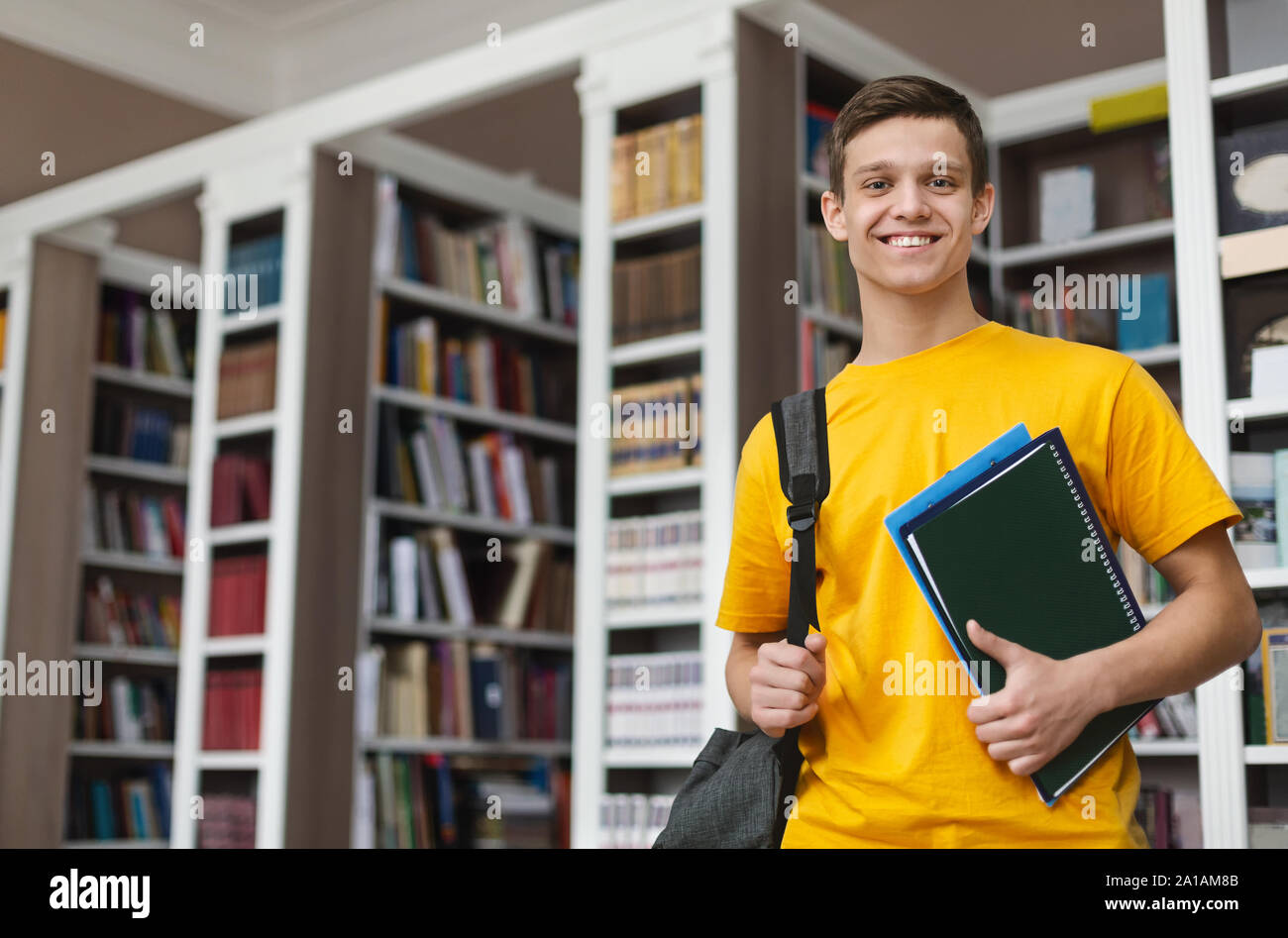 Smiling guy posing in library, holding books and notes Stock Photo