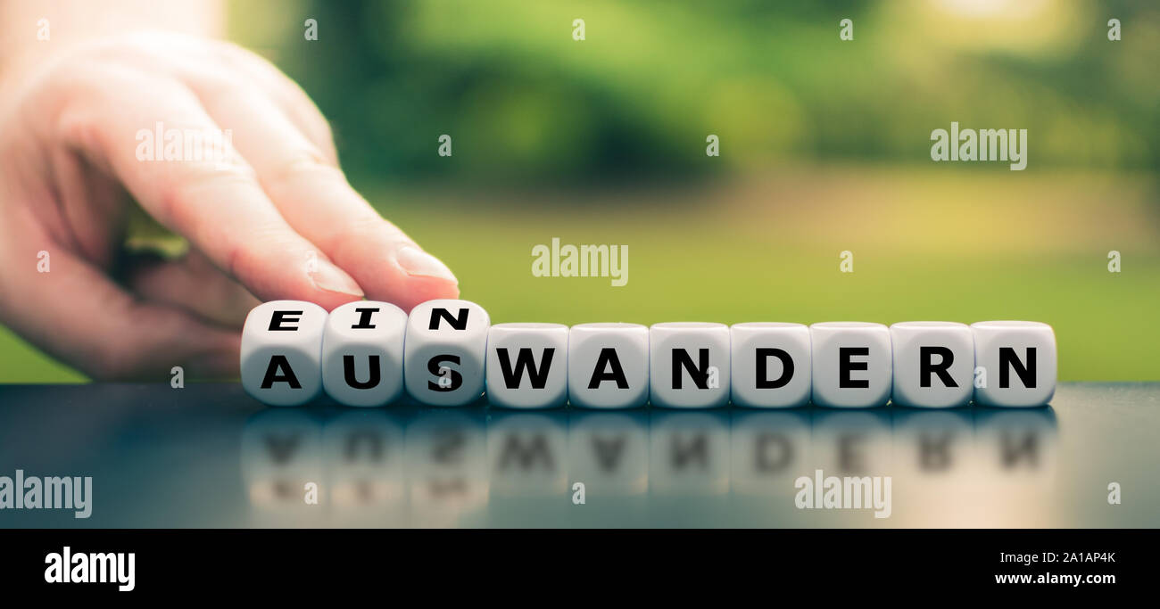 Hand turns dice and changes the German word "einwandern" ("immigrate" in English) to "auswandern" ("emigrate" in English), or vice versa. Stock Photo
