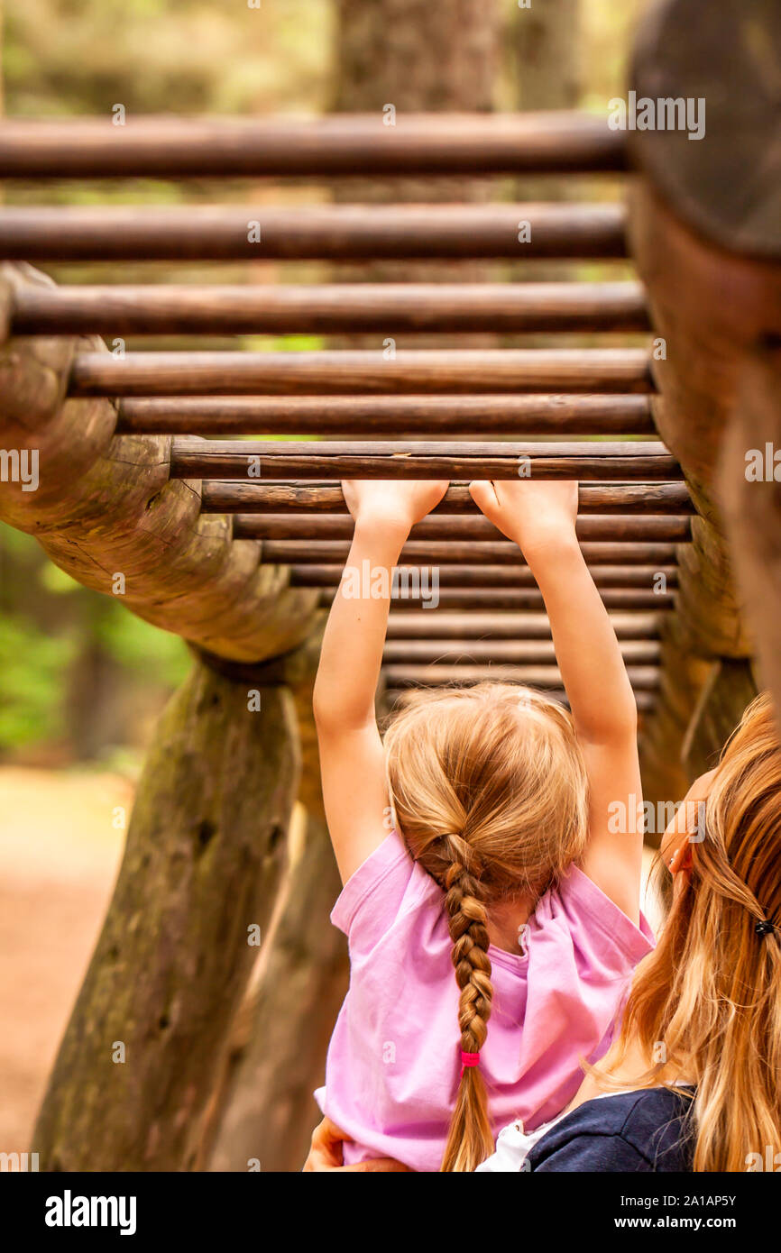 Mother Supporting daughter in the playground with climbing and hanging on a ladder. Stock Photo