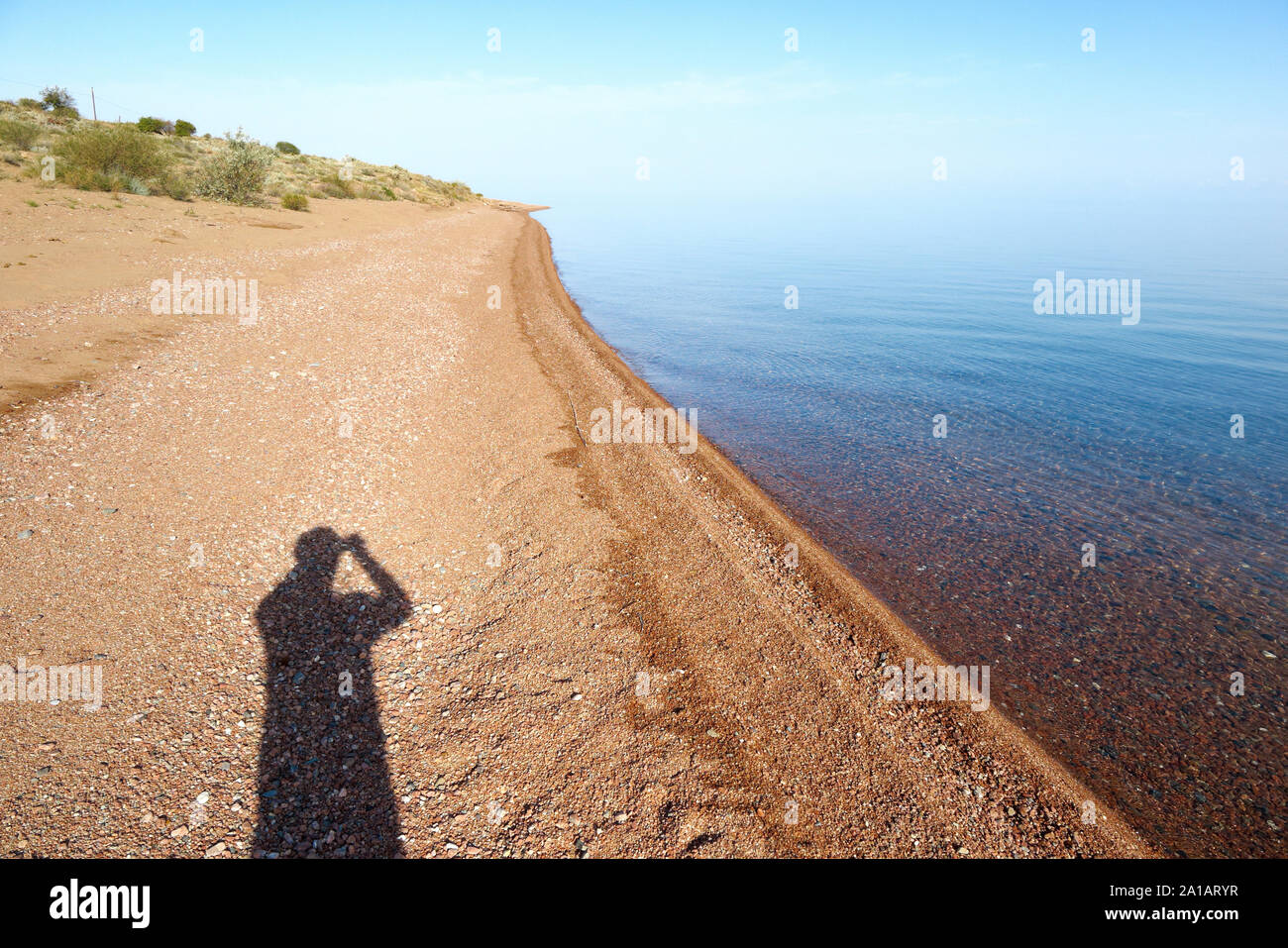 A very calm water of the Issyk-Kul lake and figure of photographer. Stock Photo