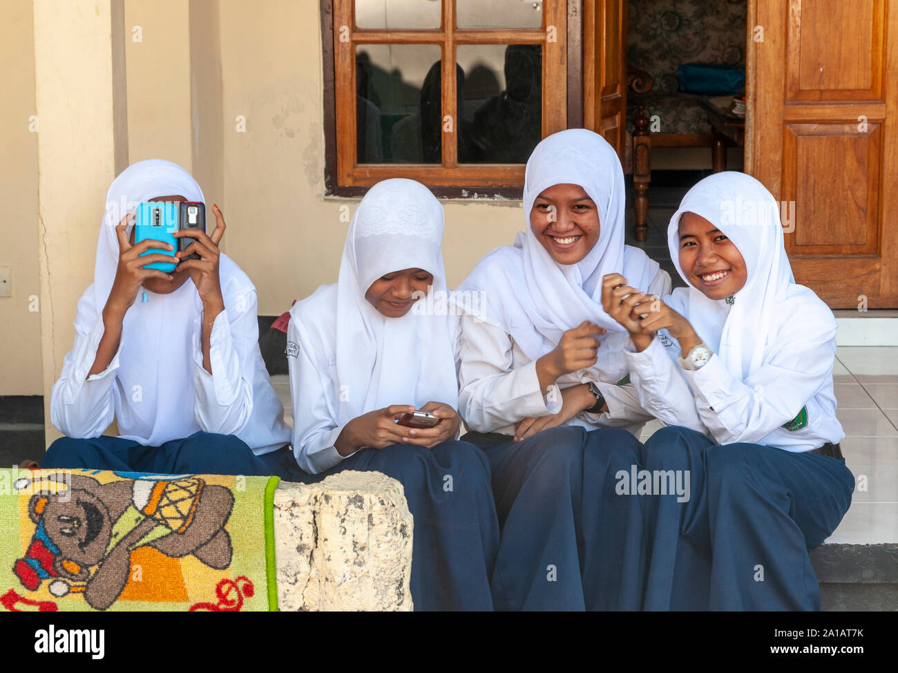Muslim school girls playing with their mobile phones,  Lovina, Northern Bali, Indonesia. Stock Photo