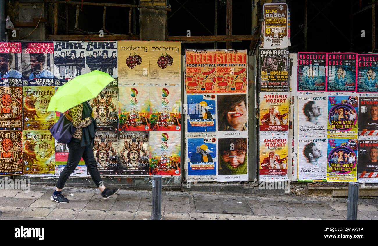 A woman walks past a wall of entertainment posters in central Athens, Greece Stock Photo