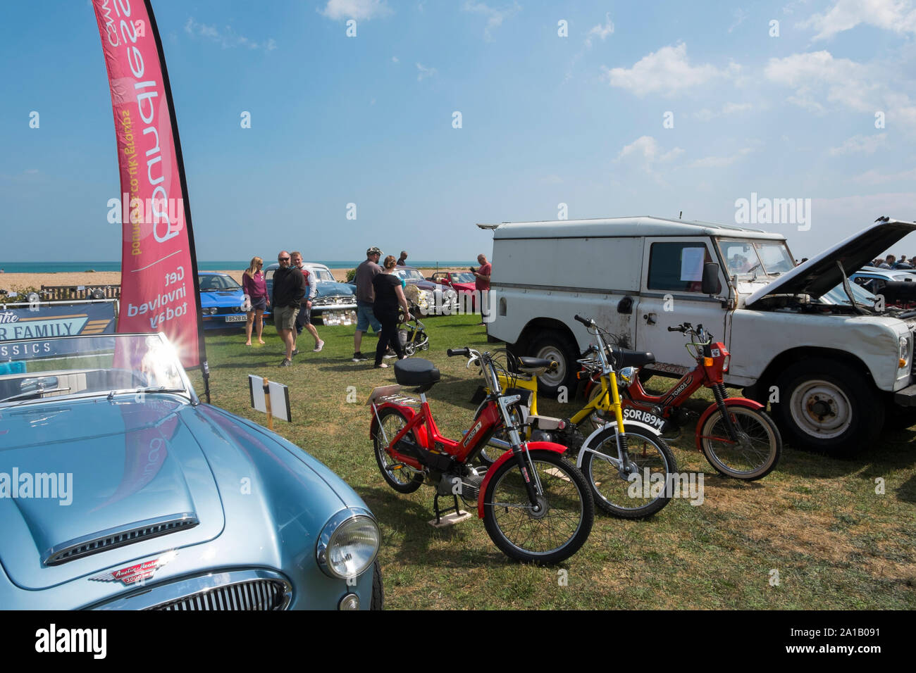 1970s Puch and Tomos mopeds next to a 1950s Austin Healey 3000 Mkll and a Land Rover at the  Deal Classic Motor Show on Walmer Green by the beach, Dea Stock Photo