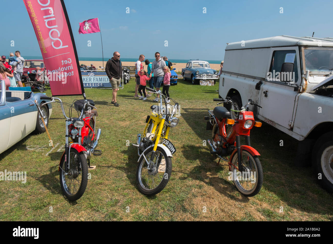 1970s Puch and Tomos mopeds next to a 1950s Austin Healey 3000 Mkll and a Land Rover at the  Deal Classic Motor Show on Walmer Green by the beach, Dea Stock Photo