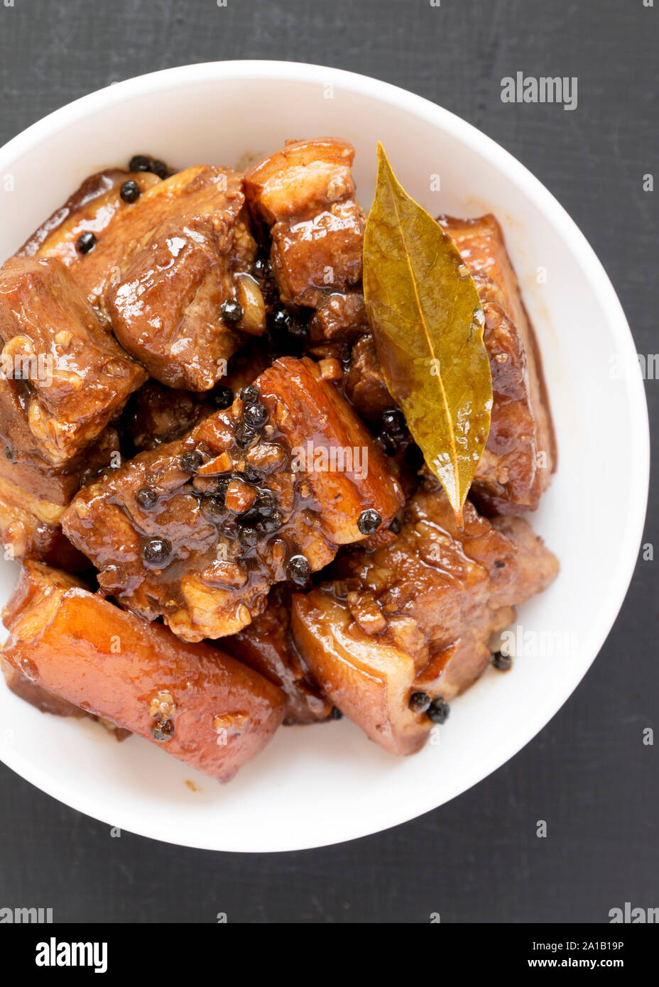 Homemade Filipino Adobo Pork in a white bowl on a black background, top