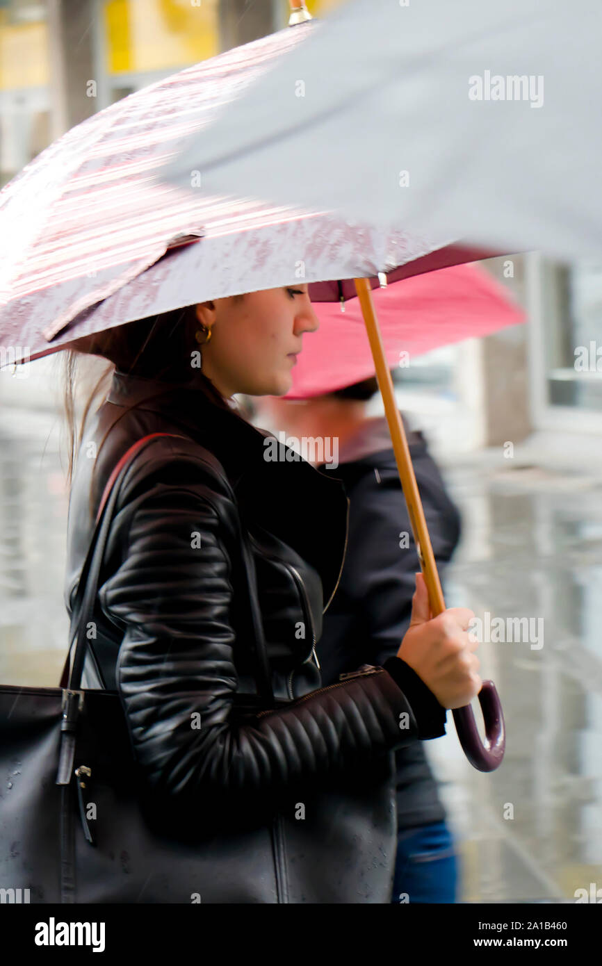Belgrade, Serbia- September 24, 2018: Blurry young woman walking fast under the umbrella on rainy and crowd city street Stock Photo