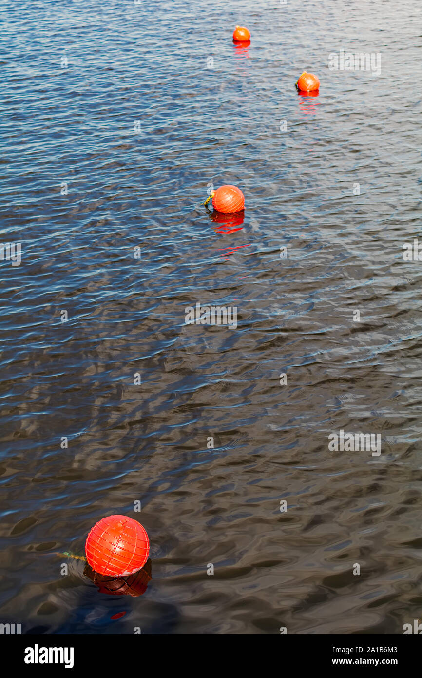 Four bright orange buoys floating on river water surface. Set of four orange safety buoys stretching into the distance in a river with small waves on Stock Photo