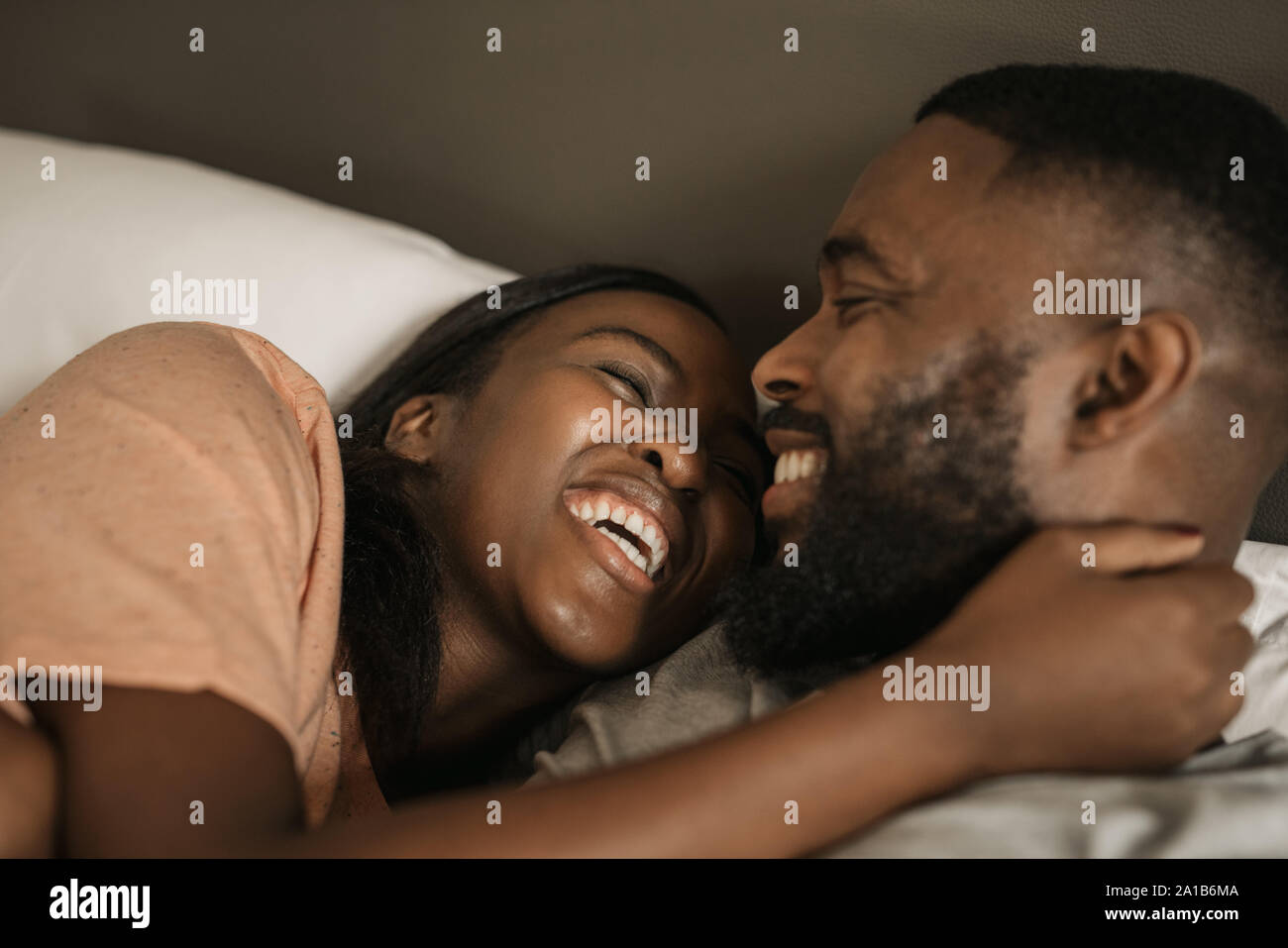 Affectionate young African American couple laughing together in bed Stock Photo