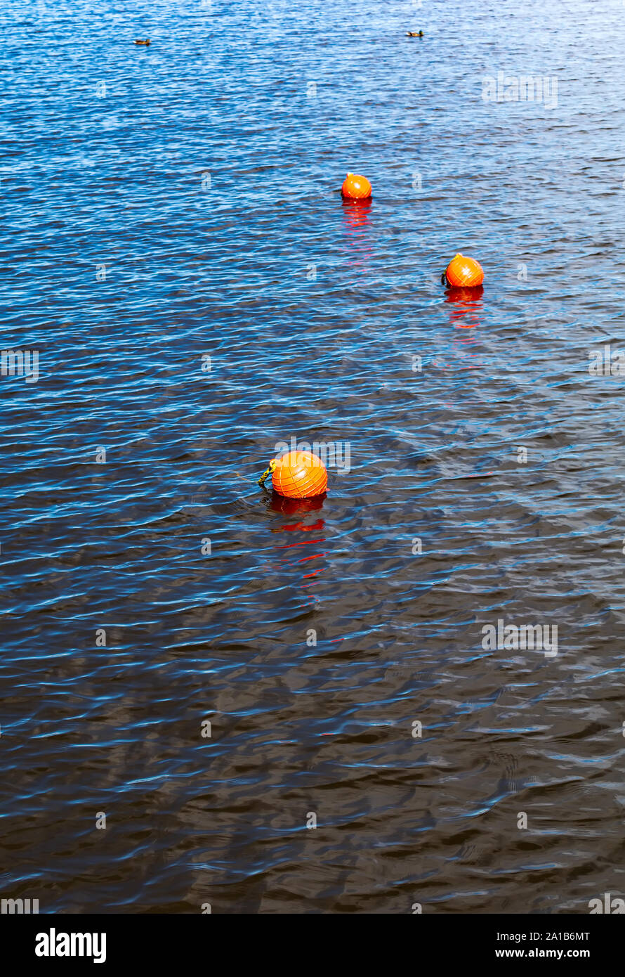 Three bright orange buoys floating on river water surface. Set of three orange safety buoys in a river with small waves on water surface. Stock Photo