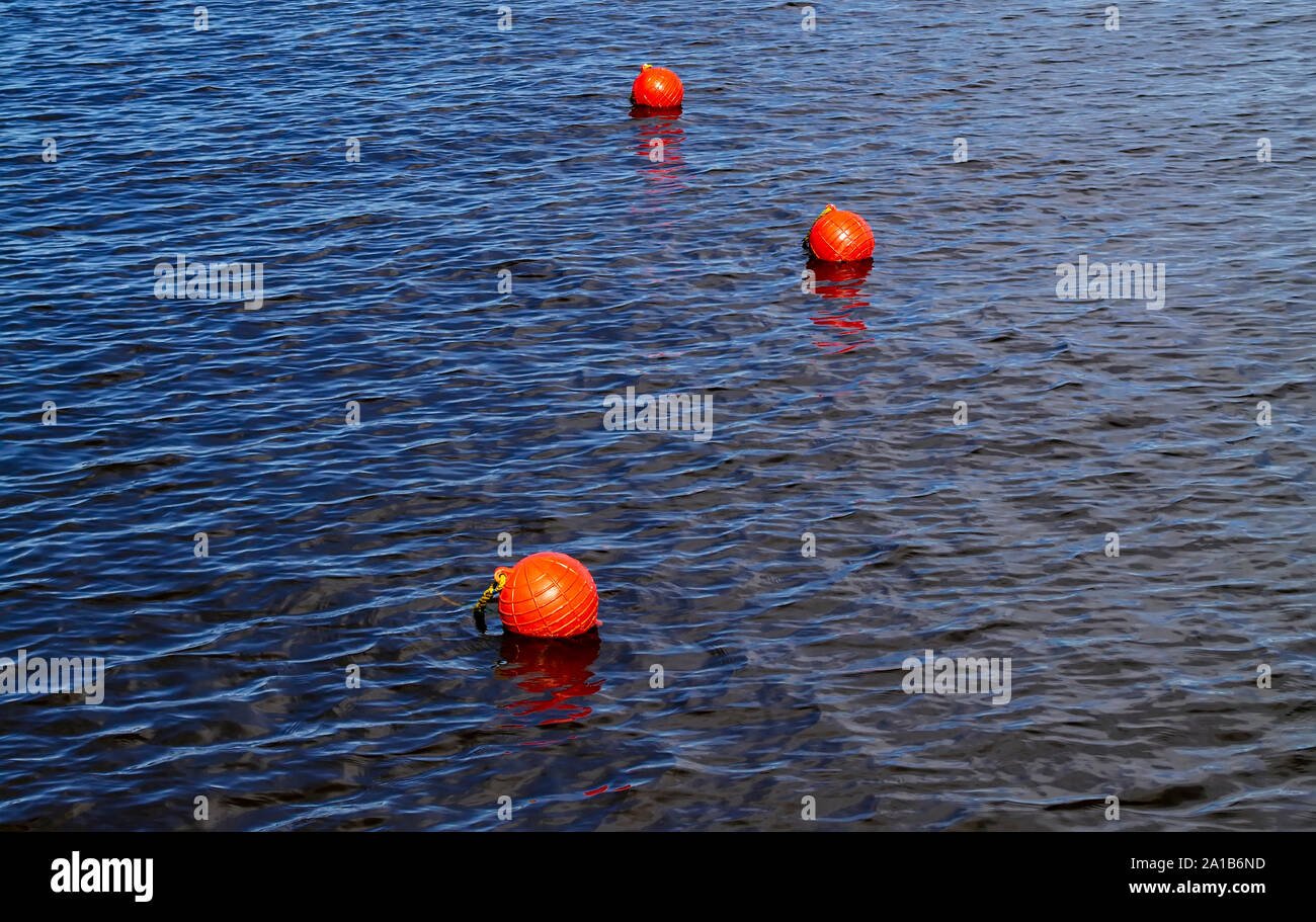 Three bright orange buoys floating on river water surface. Set of three orange safety buoys in a river with small waves on water surface. Stock Photo