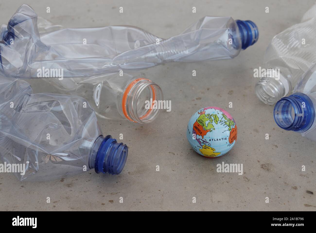 Pet plastic bottles pointing at planet earth globe on grey surface. Showing plastic pollution, recycling and zero waste concepts. Stock Photo