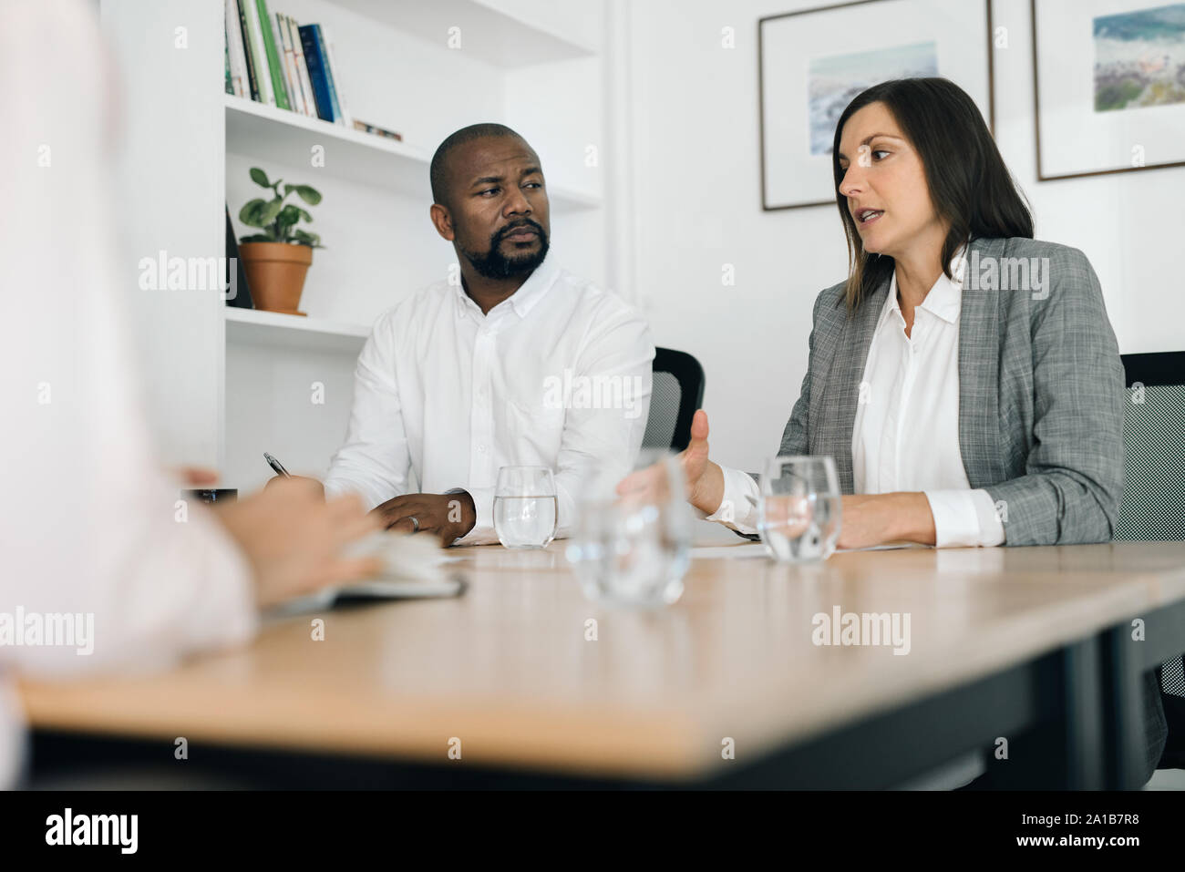 Two businesspeople talking with a colleague at an office table Stock Photo
