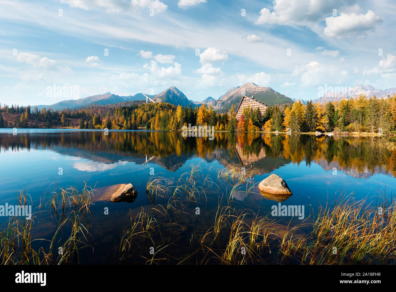 Dramatic cloudy sky under orange larch forest. Mountain lake Strbske pleso in National Park High Tatra, Slovakia, Europe. Stock Photo