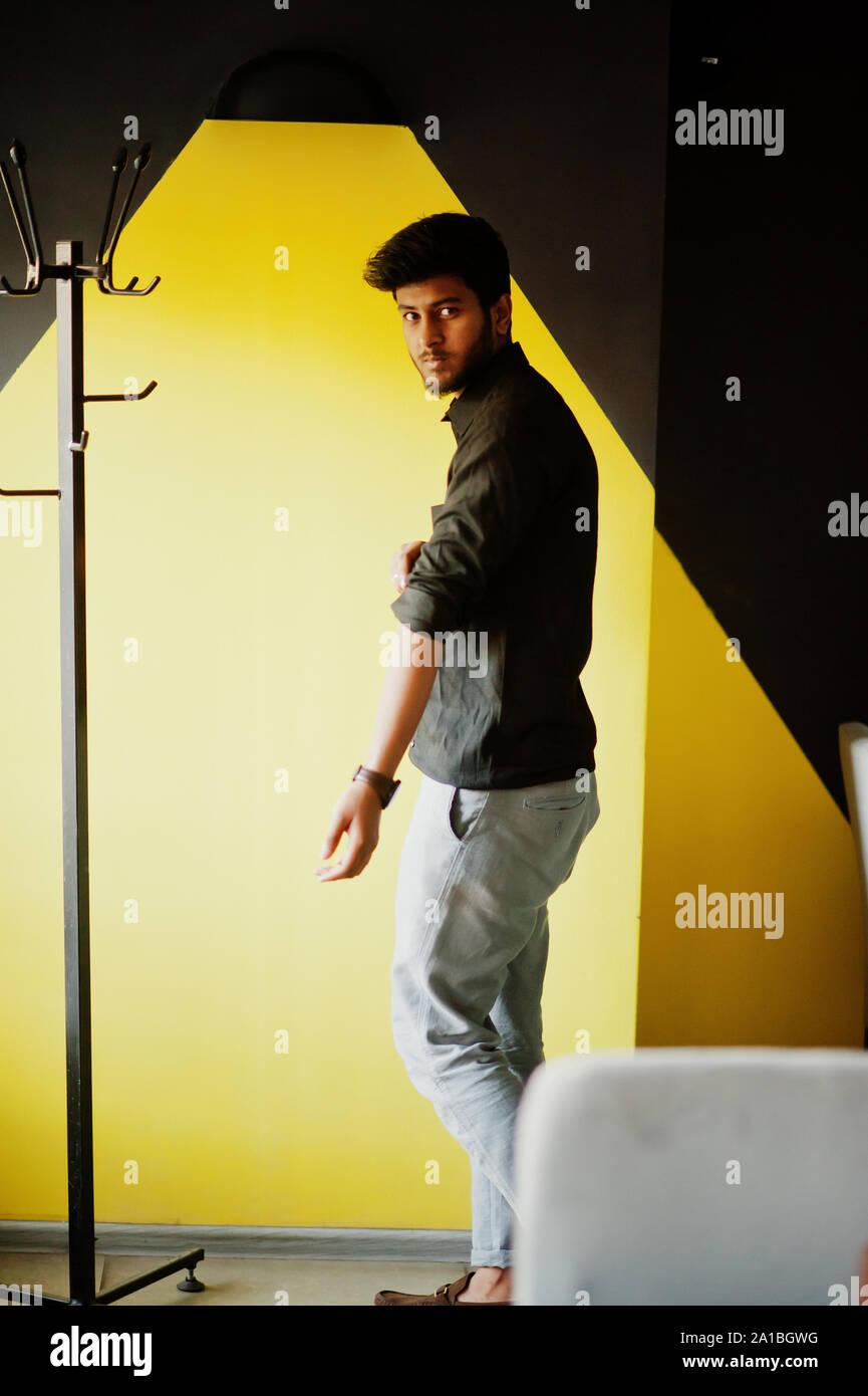Confident young indian man in black shirt standing near yellow wall ...
