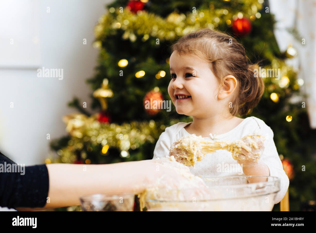 Happy little girl helping make dough and laughing in front of a christmas tree Stock Photo