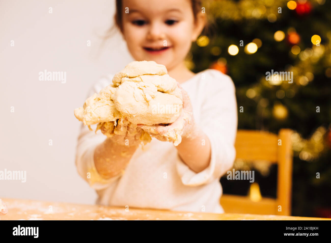 Toddler girl holding dough in front of christmas tree Stock Photo