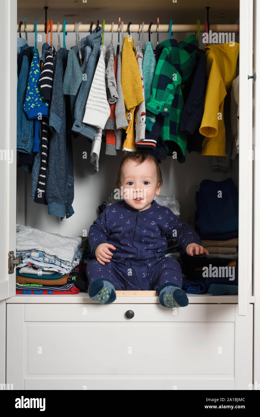 Smiling kid hiden in clothing closet filled with coloured clothes Stock Photo