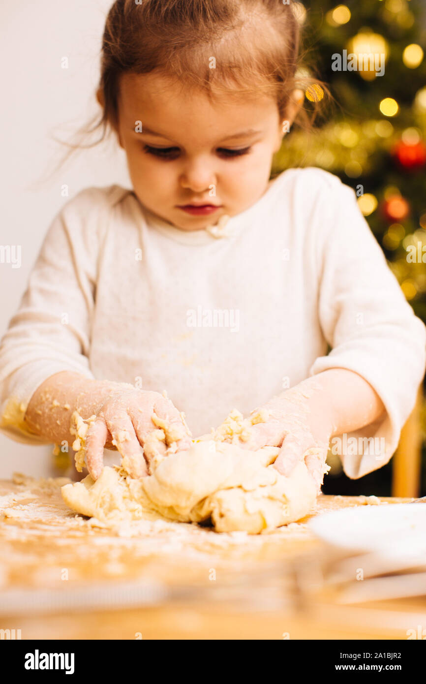 Toddler girl kneading dough in front of christmas tree Stock Photo