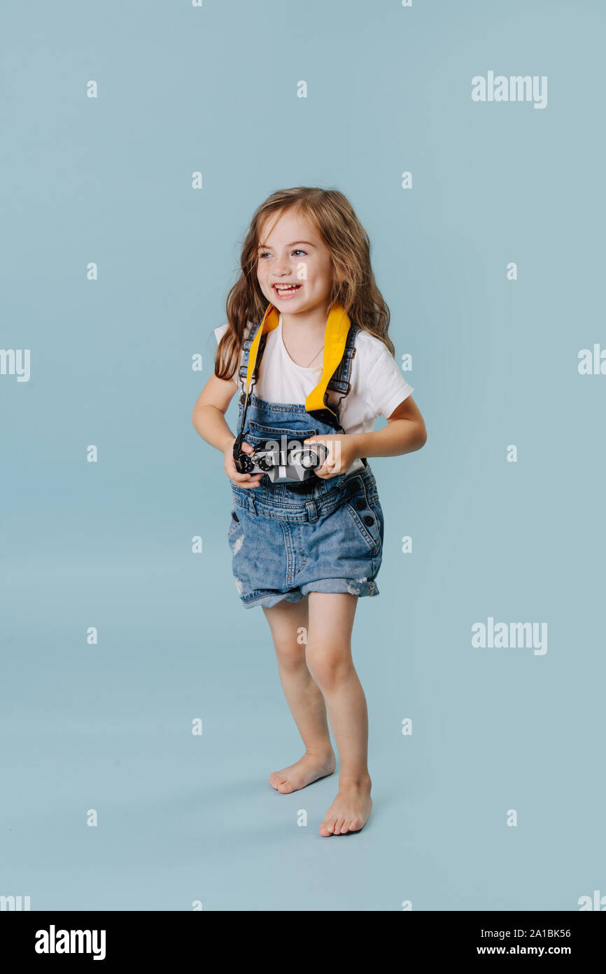 Happy little girl holding a vintage mirrored camera over blue background. Stock Photo