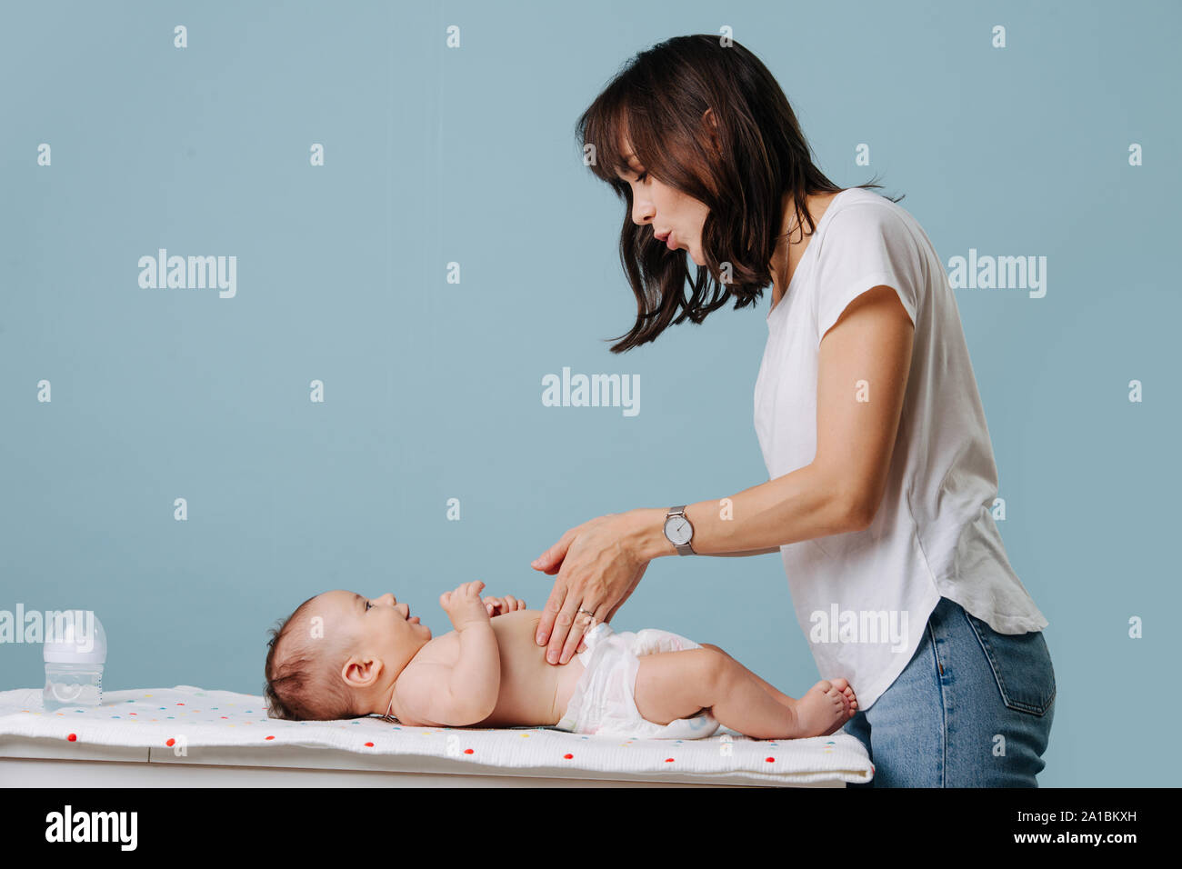 Palping Mother palping baby's stomach on table while talking to him over blue ...